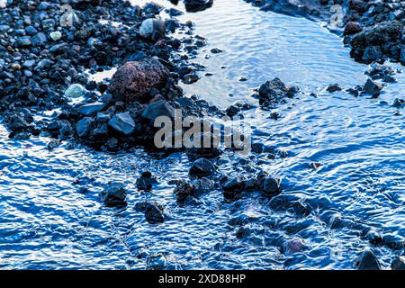 Eine felsige Küstenlinie mit einem Wasserkörper im Vordergrund. Das Wasser ist trüb und die Felsen sind überall verstreut Stockfoto