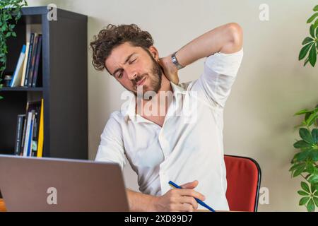 Mann, der seinen Hals schmerzhaft hält, während er an einem Laptop arbeitet – Konzepte im Zusammenhang mit Bürostress, arbeitsbedingten Beschwerden, schlechter Körperhaltung, ergonomischen Lösungen Stockfoto