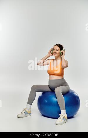 Junge schwangere Frau in aktiven Wear-Balance auf blauem Ball, tief in Musik engagiert. Stockfoto