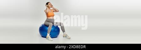 Eine schwangere Frau in Activewear sitzt anmutig auf einem blauen Trainingsball und zeigt Kraft und Gleichgewicht. Stockfoto