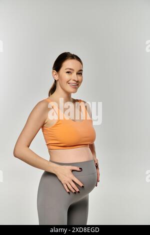 Eine schwangere Frau in Sportübungen vor grauem Hintergrund. Stockfoto