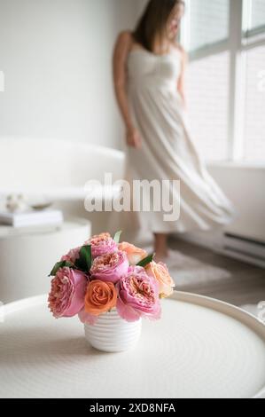 Vase mit rosa und orangen Rosen auf einem Tisch, Frau im Hintergrund. Stockfoto