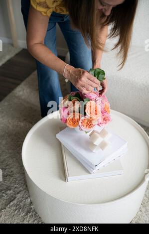 Frau, die einen Strauß rosa und orange Rosen auf einem weißen Tisch arrangiert. Stockfoto