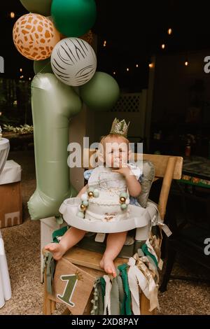Das Baby in einem Hochstuhl genießt einen ersten Geburtstagskuchen Stockfoto