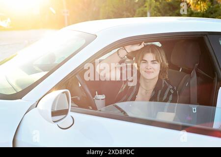 Junger Mann, der in einem weißen Auto sitzt und mit Su in die Kamera lächelt Stockfoto