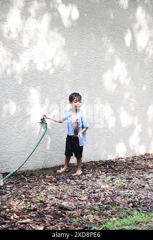 Junge, der mit einem Gartenschlauch spielt, barfuß im Y steht Stockfoto