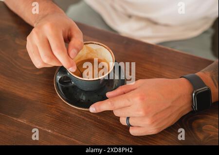 Nahaufnahme eines Mannes, der Espresso in einer Tasse am Küchentisch rührt Stockfoto