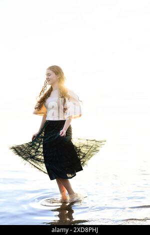 Eine junge Frau mit lockigen Haaren, die im flachen Wasser läuft, während sie ho Stockfoto