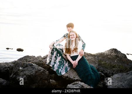 Zwei Schwestern sitzen auf Felsen und schauen ruhig in die Kamera Stockfoto