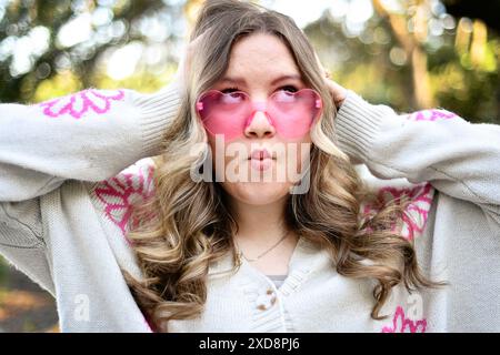 Lustig, Frau mit blonden Haaren macht ein verspieltes Gesicht, trägt Herz... Stockfoto