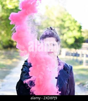 Eine Frau in einer schwarzen Lederjacke, die draußen rosa Rauch hält Stockfoto