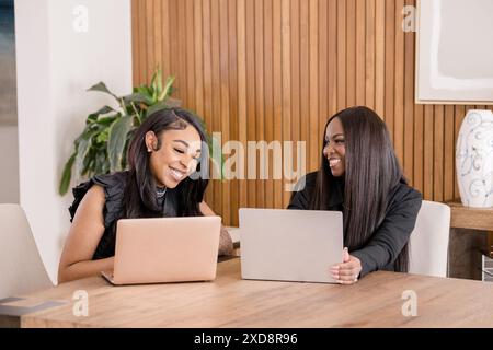 Zwei lachende schwarze Frauen, die an ihren Laptops arbeiten Stockfoto