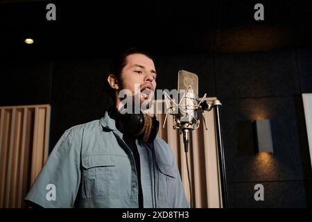Ein Mann singt leidenschaftlich in ein Mikrofon in einem Aufnahmestudio während einer Musikbandprobe. Stockfoto