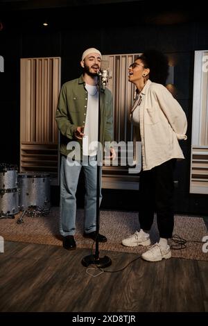 Zwei Sänger stehen in einem Aufnahmestudio neben dem Mikrofon und bereiten sich auf eine Musikbandprobe vor. Stockfoto