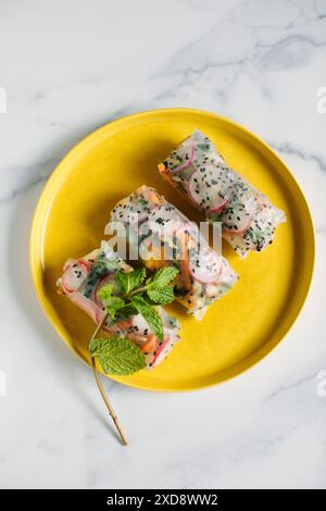 Drei frische Frühlingsrollen auf einem gelben Teller mit Minzgarnitur. Stockfoto