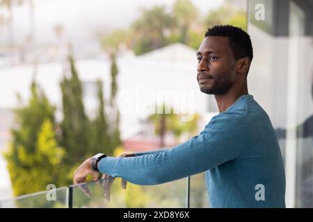 Auf dem Balkon stehend, Afroamerikaner in blauem Pullover, der in die Ferne blickt Stockfoto