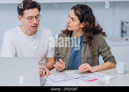 Ein Paar, das über einen Tisch mit Laptop und Kaffeetasse diskutiert, plant sein zukünftiges Zuhause. Mann und Frau planen, die Wohnung zu renovieren, das Projekt mit dem Designer zu koordinieren. Stockfoto