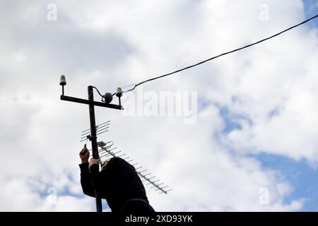 Man's Hand verbindet Kabel mit 4G Antenne Nahaufnahme mit Himmel im Hintergrund. Techniker repariert Antenne, Mann repariert TV-Signal. Wartungsarbeiten auf dem Dach Stockfoto