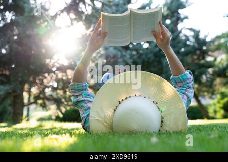 Eine junge Frau mit Strohhut verbringt gerne Zeit damit, ein Buch im Park zu lesen Stockfoto