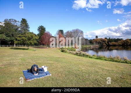 Centennial Park mit See und Model freigelassener Frau, die auf einem Picknickteppich auf dem Gras streckt, Randwick, Sydney, NSW, Australien Stockfoto