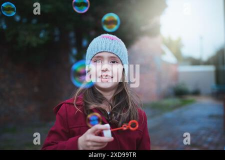 Kinder, fröhliche und blasende Blasen für Outdoor-Spiele mit Urlaubsspaß im Winter, in der Kindheit oder in der Entwicklung. Mädchen, Kind und lächelnd draußen in Kälte Stockfoto