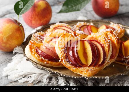 Gebackener Pfirsich in Blätterteig in Herzform mit Reifen Früchten und Marmelade in Nahaufnahme auf einem Teller auf dem Tisch. Horizontal Stockfoto