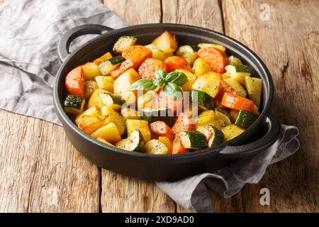 Köstliches frittiertes Gemüse, Kartoffeln, Karotten, Zucchini und Knoblauch und Kräuter aus nächster Nähe in einer Pfanne auf einem Holztisch. Horizontal Stockfoto