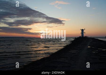 Altmodische Windmühle am felsigen Pier an der Küste der Insel usedom entlang der ostsee von Polen mit wunderschönem romantischen Sonnenuntergang und dramatischem Stockfoto