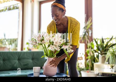 Porträt einer lächelnden Frau, die zu Hause eine Vase mit Blumen hält Stockfoto