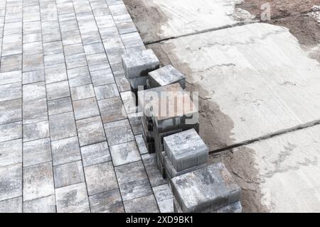 Straßenpflasterarbeiten werden ausgeführt. Graue Pflasterplatten liegen auf einer verdichteten Sand-Zement-Mischung. Hintergrundfoto mit selektivem Fokus Stockfoto