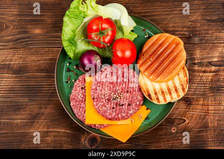 Rohe Burgerpasteten, Käse, Gemüse und Burgerbrötchen zum Kochen auf hölzernem Hintergrund. Stockfoto