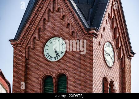 Kirchturm aus rotem Backstein mit Uhrenzifferblatt und römischen Ziffern Stockfoto