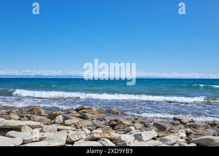 Steinküste des Südufers des großen Sees Issyk-Kul, Sommerurlaub in Kirgisistan. Klarer blauer Himmel, smaragdfarbenes Wasser aus Teich, kleine Welle. Kirgizi Stockfoto