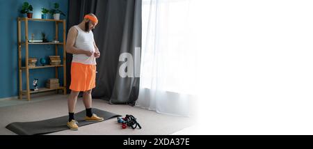 Ein Mann bereitet sich auf ein Workout zu Hause vor, gekleidet in orangefarbenen Shorts und einem Stirnband Stockfoto