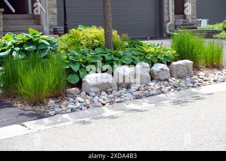 Wartungsarme vordere Gartenanlage mit dekorativem Rüstungsstein und Flussfelsen, ohne Rasen und pflegeleichten Stauden und Ziergräsern. Stockfoto