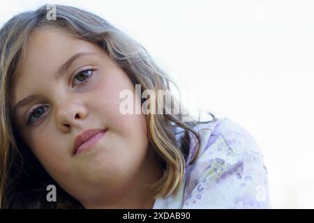 Nahaufnahme eines schönen kleinen Mädchens in einem bunten Kleid, das auf dem Gras liegt und auf die Kamera mit weißem Hintergrund und Kopierraum blickt Stockfoto