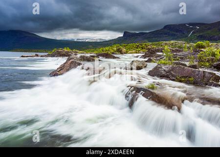 Das Bild zeigt einen atemberaubenden Wasserfall im Stora Sjöfallet Nationalpark in Schweden. Das Wasser fließt über Felsen und kaskadiert in einen See und schafft eine ruhige Atmosphäre Stockfoto