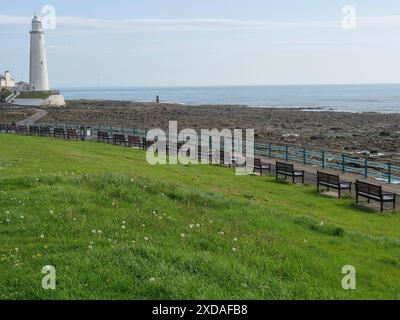 Ein weißer Leuchtturm am Meer, entlang eines Küstenweges mit Bänken und grünem Gras. Eine ruhige und sonnige Atmosphäre, von hier aus, england, Großbritannien Stockfoto