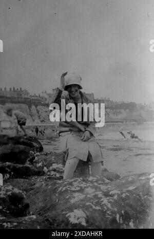 Eine Dame mit Hut und Mantel, die an einem windigen Junitag auf einem Felsen am Wasserrand sitzt. Mode und Kultur. Aus einer Sammlung von Schnappschussfotos einer Gruppe von Frauen, 1928. Es gab nur wenige Anmerkungen auf den Fotos, aber die Frauen schienen als Gruppe zu reisen und hatten eindeutig eine Vorliebe für die englische Grafschaft Kent. Einige der Fotos deuten darauf hin, dass sie Feministinnen ihrer Zeit waren, und obwohl sie weitgehend unbekannt sind, habe ich sie aufgenommen, da sie einige der Mode der Zeit repräsentieren. Stockfoto