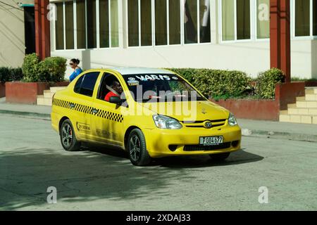 Kuba, Kuba, Zentralamerika, Yellow Taxi fährt an einem Gebäude auf einer Straße vorbei Stockfoto