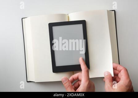 Konzept des Lesens in elektronischem Buch im Vergleich zu Papier mit eBook auf Papierbuch und Hände, die auf beiden Objekten Seite drehen. Draufsicht. Stockfoto