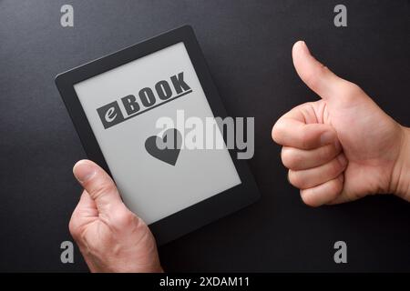 Detail der Hand, die ein eBook mit Nachricht und Herz auf dem Bildschirm und Hand mit OK-Geste isoliert auf einem schwarzen Tisch nimmt. Draufsicht. Stockfoto