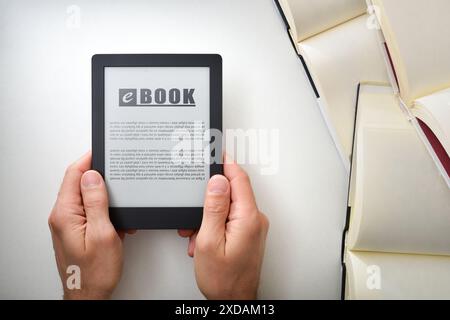 Detail der Hände, die ein eBook mit Text auf dem Bildschirm auf einem weißen Tisch voller Papierbücher aufnehmen. Lesekonzept im elektronischen Buch. Top VI Stockfoto