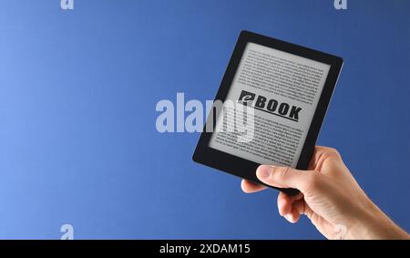 Detail der Hand, die ein eBook mit geschriebenem Text auf blauem Hintergrund nimmt. Vorderansicht Stockfoto