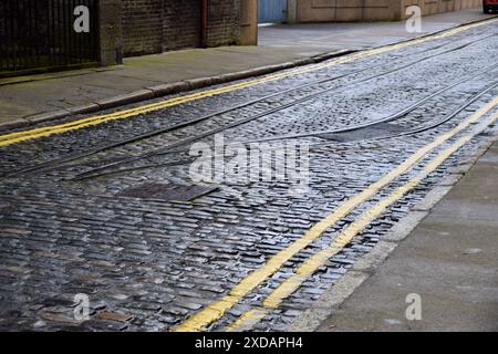 Alte Bahngleise auf einer Kopfsteinpflasterstraße in Dublin, Irland. Doppelte gelbe Linien nebeneinander. Stockfoto