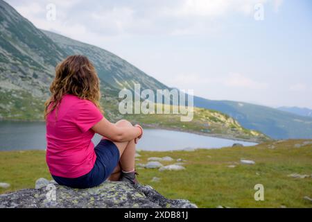 Ein Mädchen, das auf einem großen Felsen über dem Bucura-See sitzt, Retezat-Nationalpark, Rumänien Stockfoto