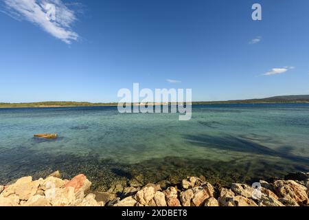 Atemberaubende Aussicht auf Cala de Fornells auf Menorca, mit kristallklarem türkisfarbenem Wasser, felsiger Küste und einem Segelboot am Horizont unter einem hellen Licht Stockfoto