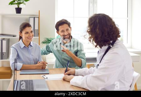 Glückliches junges Paar, das mit einem männlichen Hausarzt Therapeuten in der medizinischen Klinik sitzt. Stockfoto