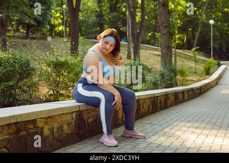 Müde, übergewichtige Frau, die sich nach einem Joggingtraining im Park auf einem Steinrand entspannt Stockfoto