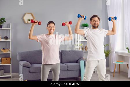 Ein Paar trägt Sportkleidung und macht zusammen mit Kurzhanteln zu Hause sportliche Übungen. Stockfoto